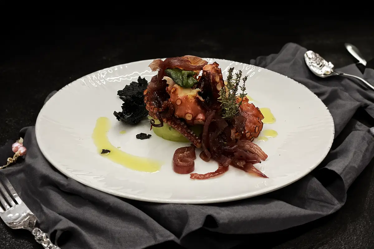 Tentacoli di polipo su patata al basilico, cipolla caramellata e cialda al nero di seppia